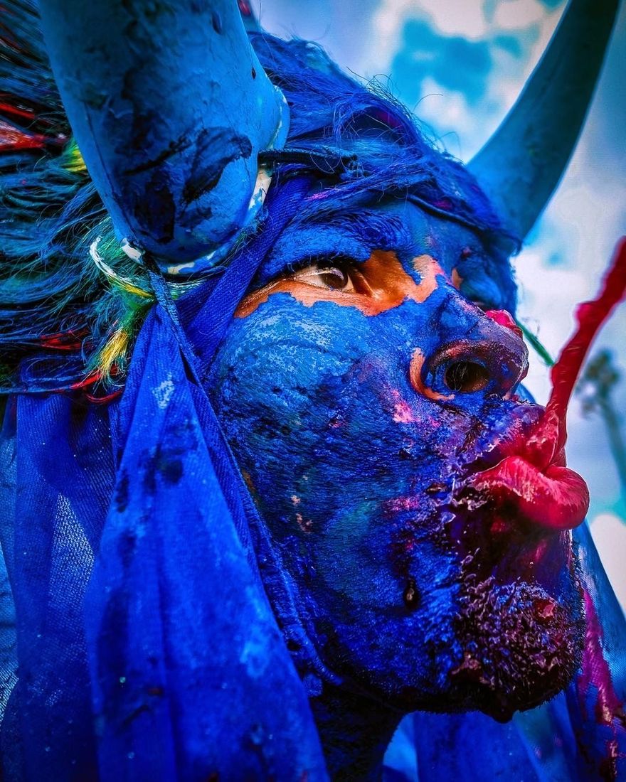 Masquerader in blue body paint and horns blowing a red kiss